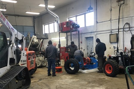 Four heavy equipment service technicians working on repairing machinery with a white Bobcat® …